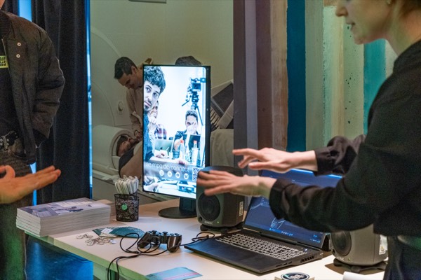 Stand auf der Science Fair: eine Forscherin erklärt an einem Bildschirm, davor liegen Flyer, Kopfhörer und ein Laptop.