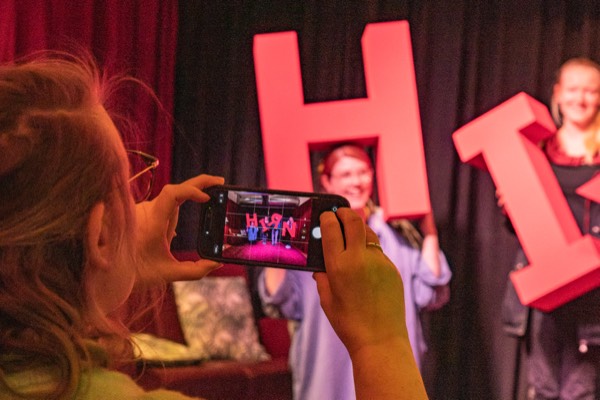 Zwei Personen halten große rote Buchstaben hoch, eine Besucherin fotografiert die Szene mit dem Handy.